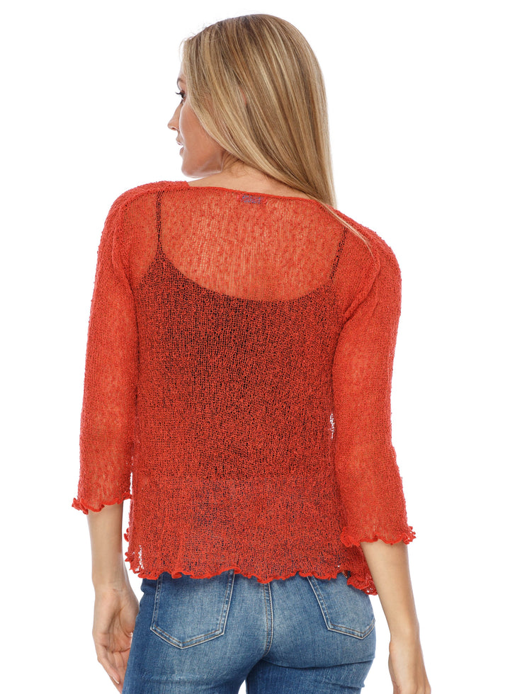 A woman shown from the back wearing a textured, sheer knit shrug by SHU-SHI in burnt orange, paired with blue jeans against a white background.