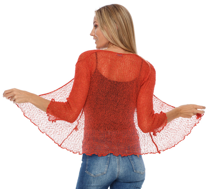 A woman shown from the back wearing a textured, sheer knit shrug by SHU-SHI in burnt orange, paired with blue jeans against a white background.