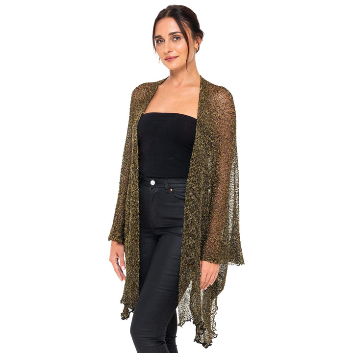 SHU-SHI black and gold metallic cardigan worn as a lightweight sparkly open-front cover-up over a black strapless top and jeans, modeled against a white studio background.