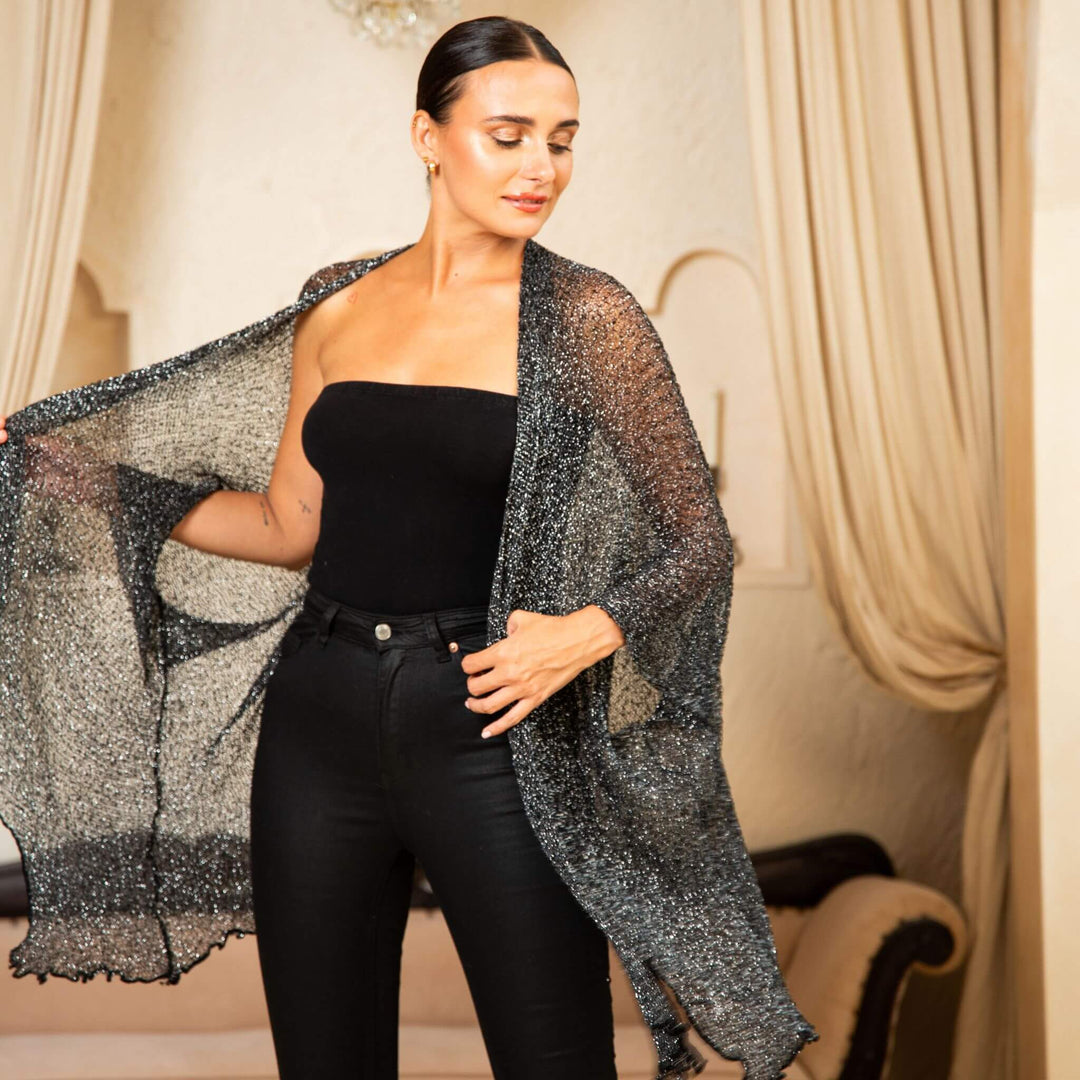 SHU-SHI black and gold metallic cardigan lightweight sheer cover up worn over a black strapless top, styled with black pants in an elegant room with cream curtains and a decorative chair.