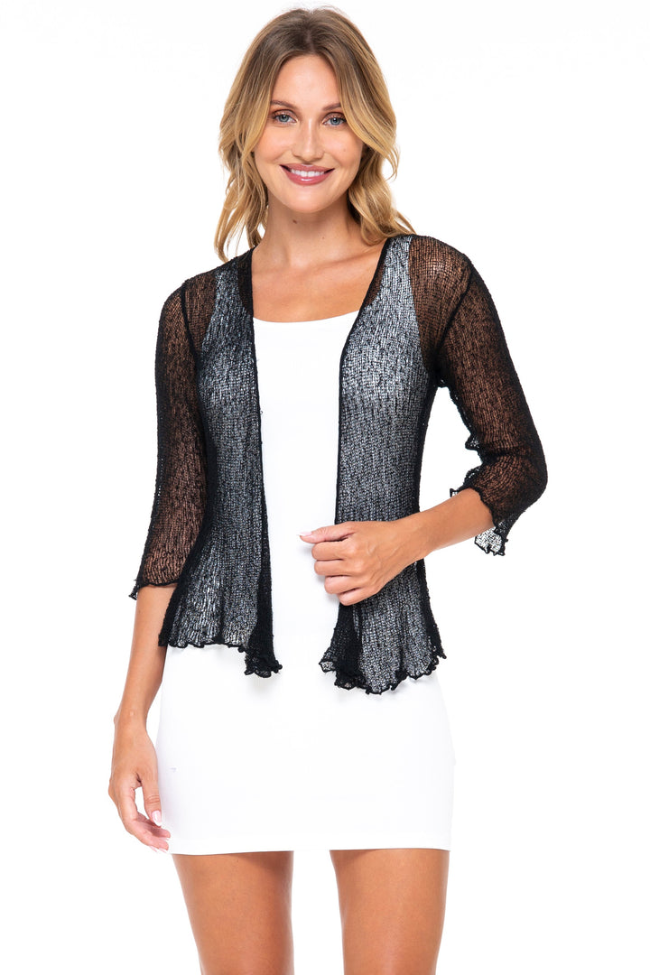 model wearing SHU-SHI open weave knit cardigan in Black over a white dress in a studio setting. 