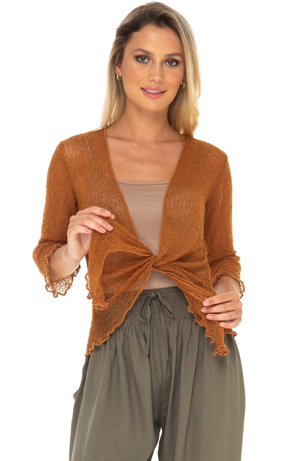 A woman modeling a SHU-SHI rust-brown open-front cardigan tied at the waist over a beige top, paired with olive green harem pants and white slide sandals, against a solid white background.