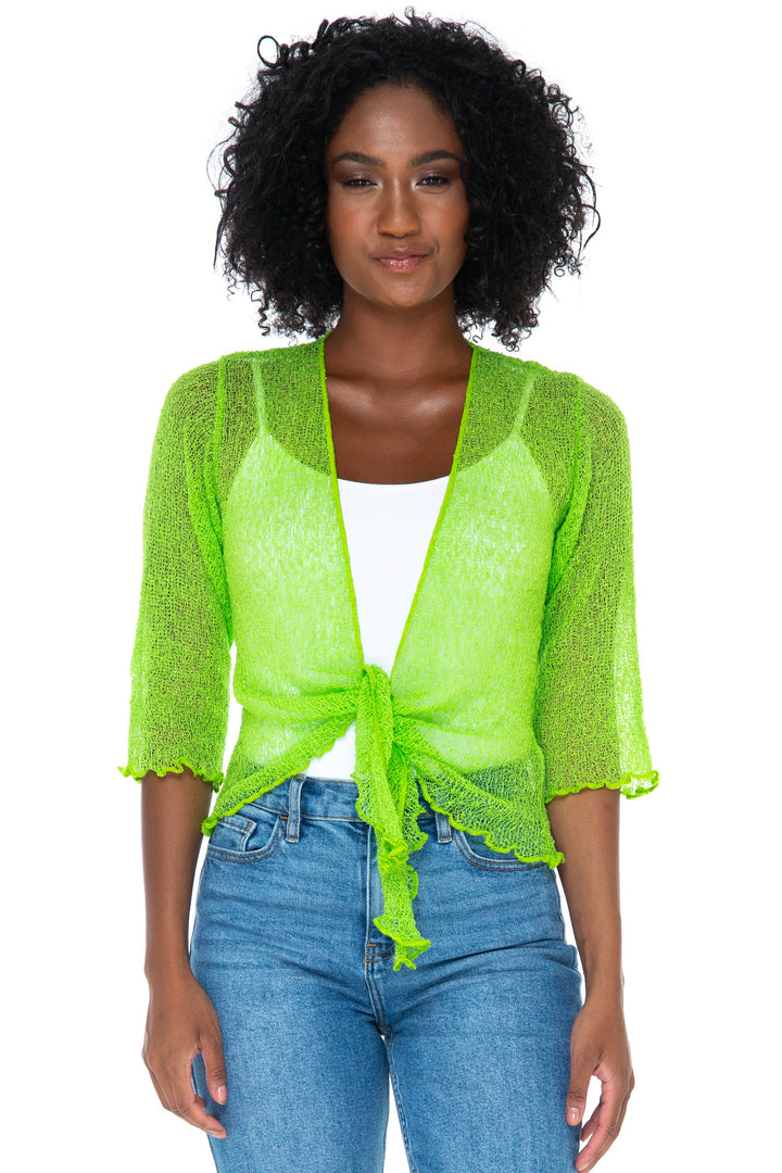 A woman modeling a SHU-SHI neon green sheer tie front open knit cardigan tied at the waist over a white top and blue jeans, standing against a plain white studio background.