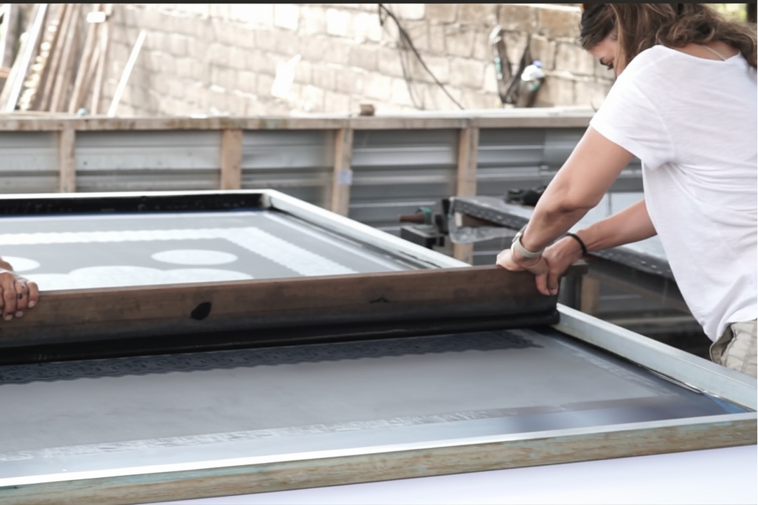 Two people working on a large screen printing frame outdoors.