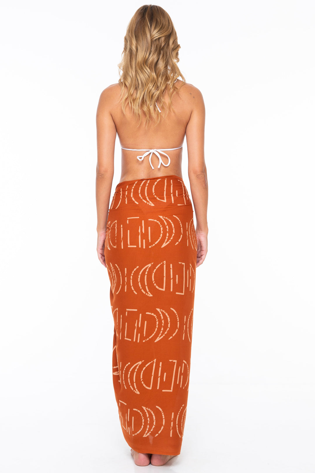 Woman wearing a white bikini top and SHU-SHI moon print sarong in Ginger on a white background - back view